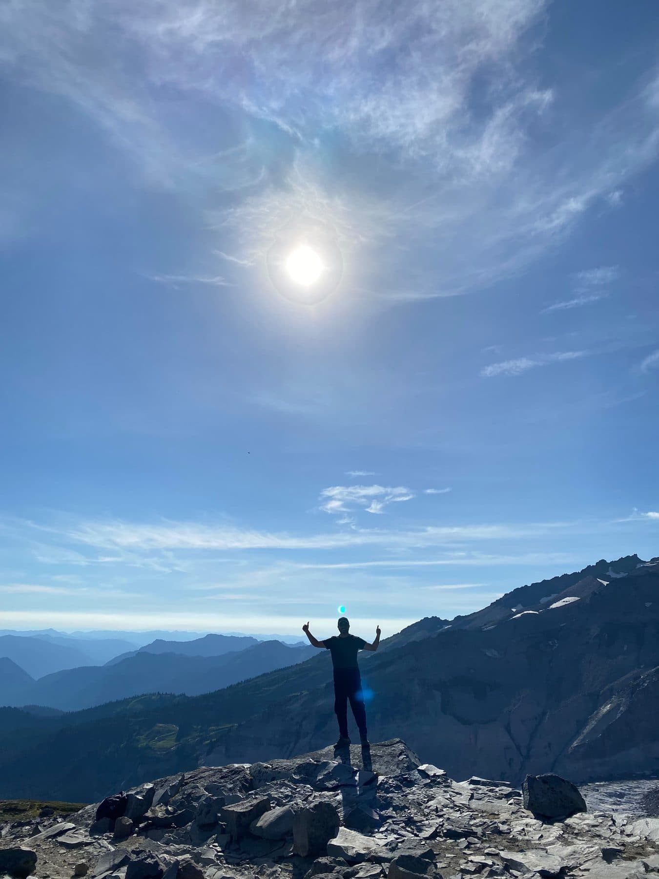 Arms raised on a rocky ridge under a haloed sun